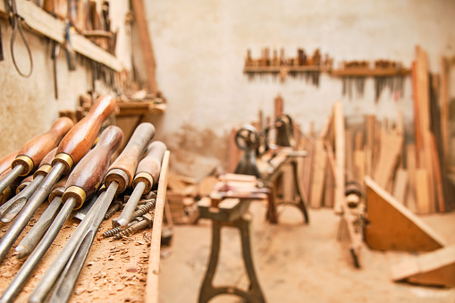 tools in the foreground of an artisan carpentry workshop with a traditional lathe out of focus in the background