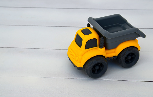 Toy childrens dump truck  on a white wooden background.Yellow and grey miniature car.Selective focus.