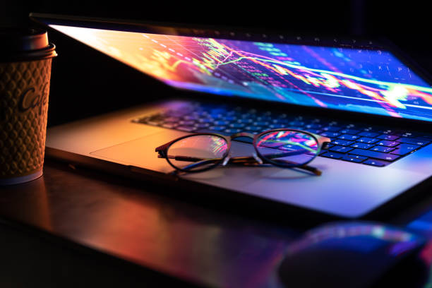 a laptop half closed in the dark with colourful glow, cup of coffee and glasses. - growth global business global communications healthcare and medicine imagens e fotografias de stock