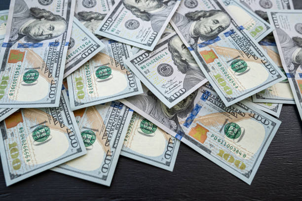 istock Pile of new 100 dollar banknotes bills on black 1488411243