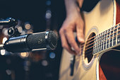 Male musician playing acoustic guitar behind microphone in recording studio.