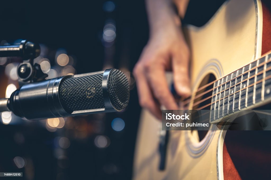 Male musician playing acoustic guitar behind microphone in recording studio. Male musician playing acoustic guitar behind microphone, close-up, recording in a music studio. Singer Stock Photo