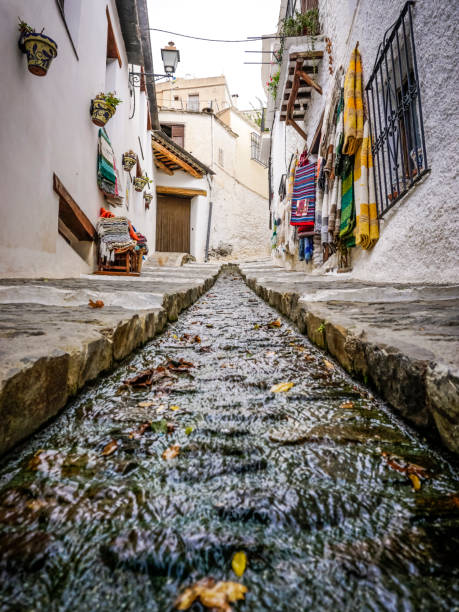 calle de un pueblo de la alpujarra granadina con agua corriendo por un canal en el centro de la carretera - alpujarra fotografías e imágenes de stock