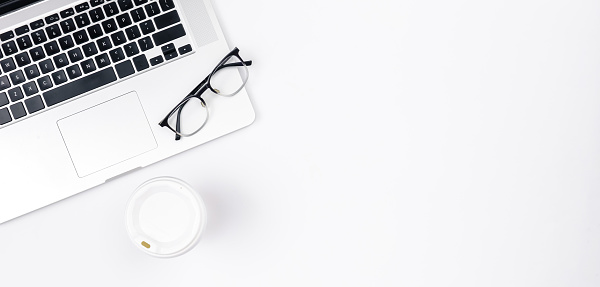 Minimalistic white background with laptop, disposable paper cup and glasses, top view, copy space.