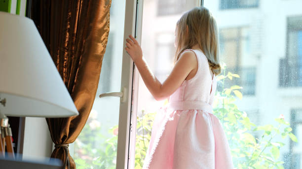 Close-up of small child standing on windowsill at open window. Danger of falling from height concept