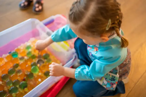 Little girl playing with sensory water beads, hydrogel balls. Sensory development and experiences, themed activities with children, fine motor skills development. High quality photo