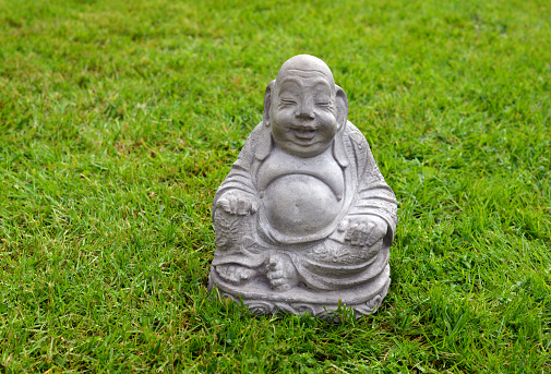 Closeup of a mass produced concrete smiling Buddha statue on a lawn in a residential yard.