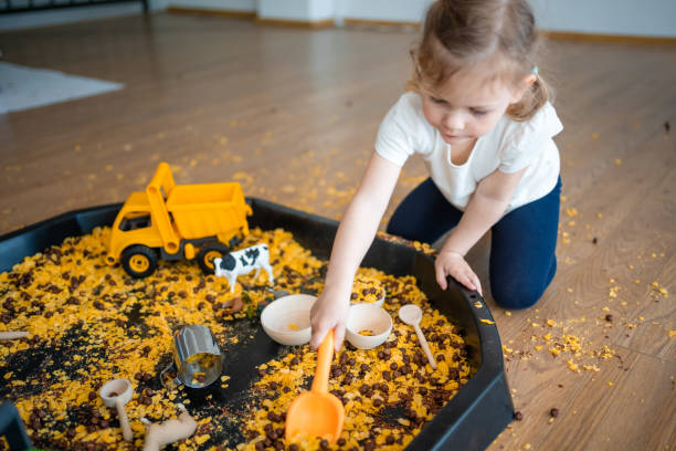 Little girl playing with sensory flakes in sandbox for playing. Sensory development and experiences, themed activities with children, fine motor skills development
