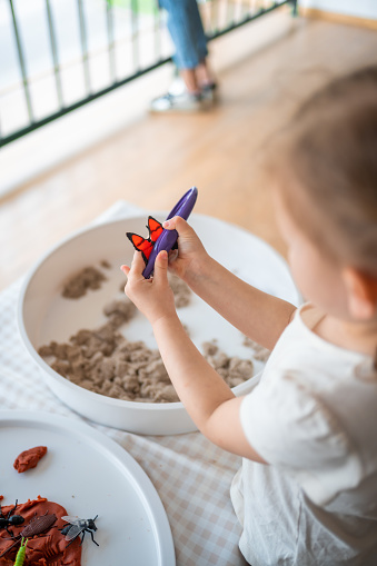 Little girl playing with kinetic sand and toys insect. Sensory development and experiences, themed activities with children, fine motor skills development. High quality photo