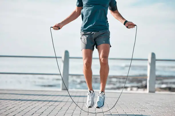 Jump rope, fitness and man by a sea promenade with training, sports and exercise equipment. Health, jumping and body wellness of a athlete doing cardio jump for active lifestyle by the ocean