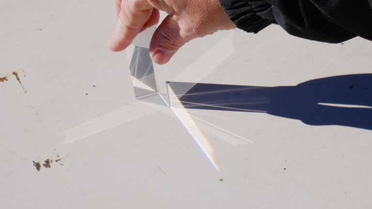 Hand moving a triangular prism in full sunlight and creating the refraction and decomposition of sunlight