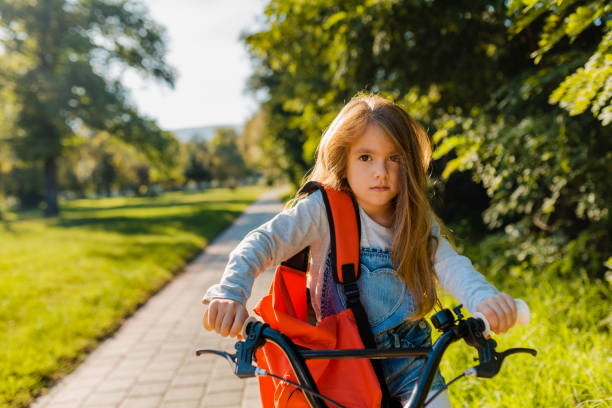 Sweet little girl with red backpack riding a bicycle in the park