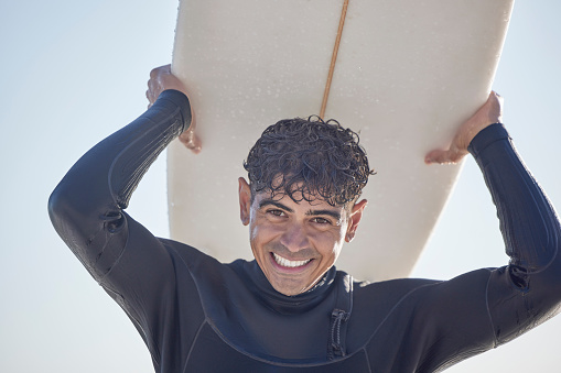 Portrait, surf and man surfer with surfboard at the beach, sea or ocean with a smile and is happy on a summer day. Exercise, surfing and male with swimsuit in Australia with freedom on the waves