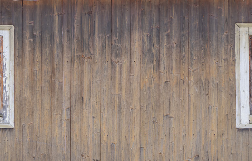 Abstract textured wooden background. Wall of house from brown wooden boards with white parts of windows. Copy space for your text and decorations. Natural construction materials theme.