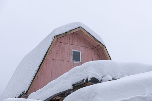 Thick layer of fresh snow lies on rooftop of wooden cabin. Overcast sky. White snowdrift on roof. Soft focus. Winter weather forecasting theme.
