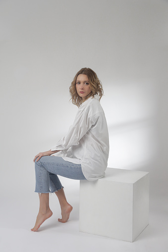 Fashion portrait of young woman in white cotton button down shirt and blue jeans on the white background
