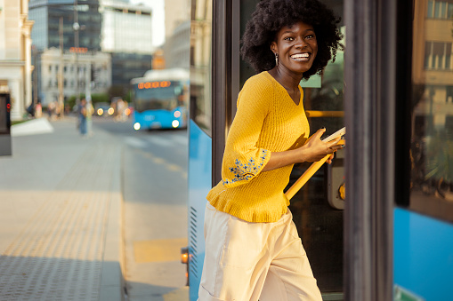 Beautiful black woman getting on the bus and looking at camera. She is happy and smiled