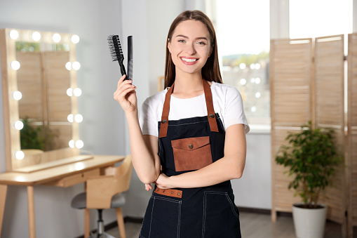 Portrait of happy hairdresser with comb and brush in beauty salon