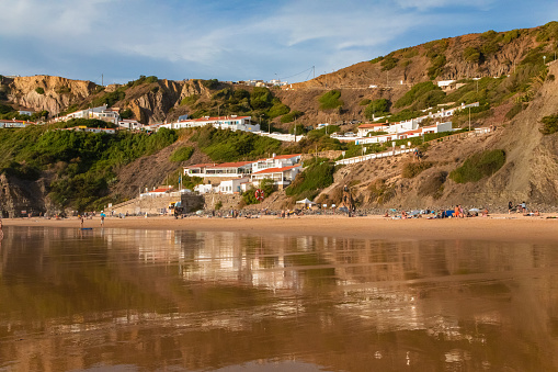 Arrifana, Aljezur, Portugal. 09. 29. 2020. best surfers places in Portugal. beautiful bay wet golden sand like a mirror, sunset. people and buildings in the distance. Surf sport wellness and travel concept