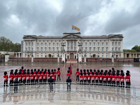 Armed soldiers are forming in the front yard at Buckingham Palace, London, England. This picture was taken from outside the palace during the changing ot The Queen's Guard, the infantry soldiers charged with guarding the official royal residences in the United Kingdom. A bearskin is a tall fur cap, usually worn as part of a ceremonial military uniform.
