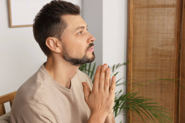 istock Man with clasped hands praying in room at home 1488438566