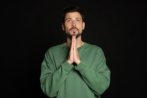 Man with clasped hands praying on black background