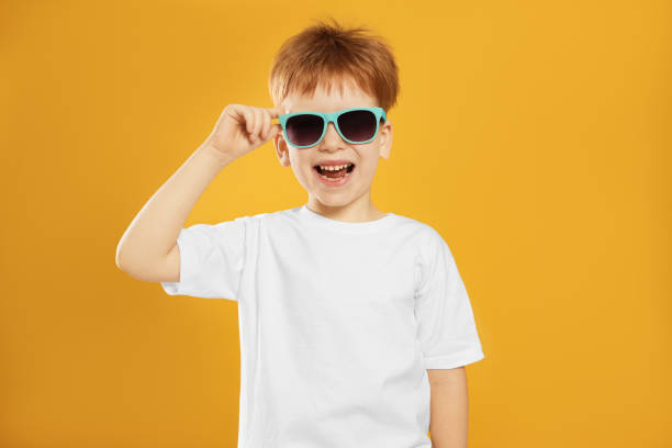 Cute little boy with sunglasses on yellow background