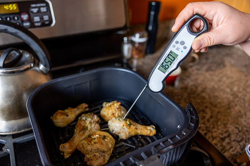 High quality stock photo of a Asian American woman cooking chicken in her kitchen demonstrating food safety by checking the temperature internally.