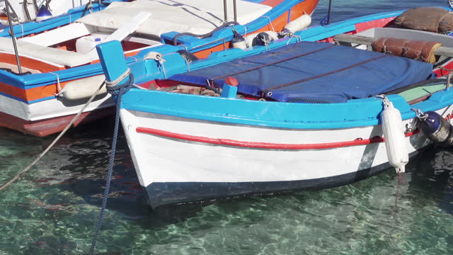 Small traditional colorful fishing boats moored with beautiful transparent turquoise blue water in summer in a resort town for summer holidays in Mediterranean sea, Italy