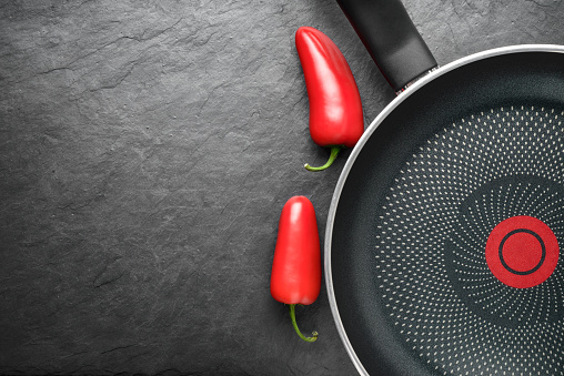 Blank skillet with non-stick coated surface on the black slate with red peppers. Empty frying pan with copy space.