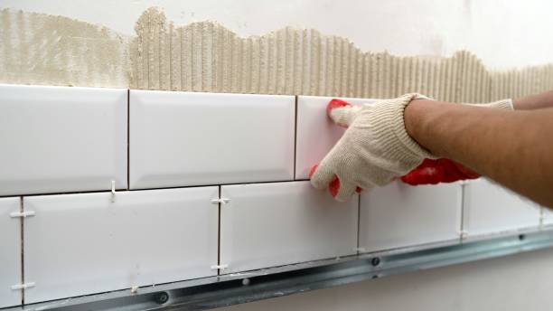 A worker lays and installs white ceramic tiles in a kitchen. Ceramic tile-fish. Laying ceramic tiles on the backsplash of the kitchen.