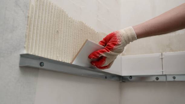 Industrial close-up of a worker's hand applying cement adhesive for laying ceramic tiles. Attaching tiles to the wall. Laying tiles on the wall. stock photo