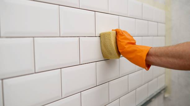 The ceramic tile laying master wipes the seams with a special sponge. Cleaning a tiled wall with a male hand with a sponge. Male hands wipe ceramic tiles with a sponge. stock photo