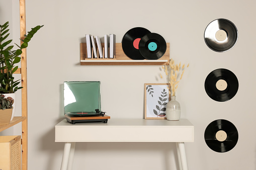 Table and stylish turntable near white wall decorated with vinyl records