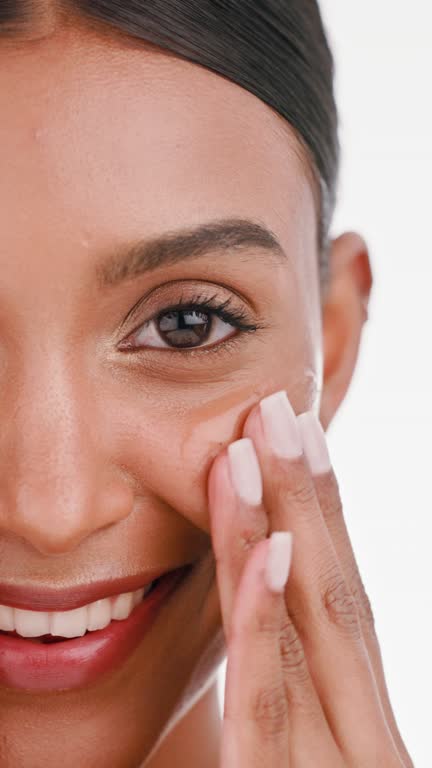 Woman, face and applying skincare cosmetics, serum or oil product for moisturizing against a white studio background. Closeup portrait of happy person smiling for beauty cosmetic or facial treatment