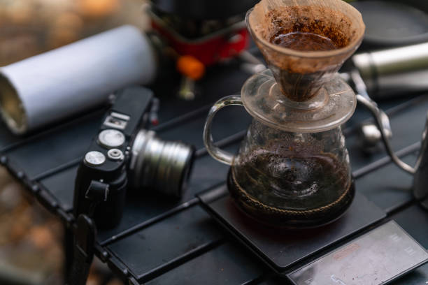 a selective focus on coffee brewer and coffee pot with camera, grinder, stove in the background stock photo