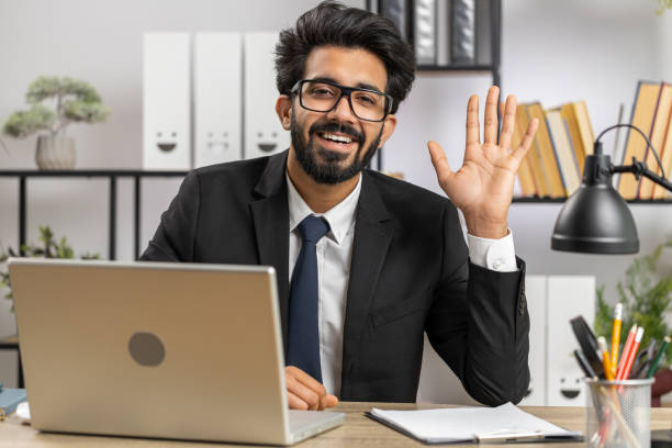 istock Businessman working on laptop smiling friendly at camera and waving hands gesturing hello at office 1488459086