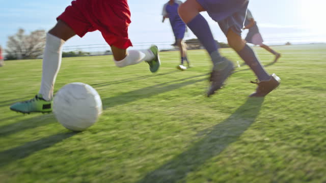 Soccer ball, shoes and children on a field for sports, kick and tackle, training and practice. Children, fitness and feet of friends playing football match, speed and energy, running and competitive