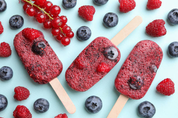 Tasty berry ice pops on light blue background, flat lay. Fruit popsicle