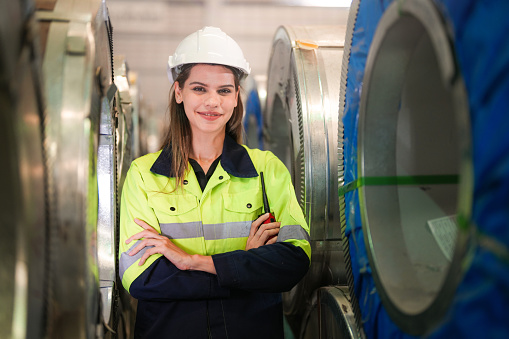 engineer woman standing with confidence with green working suite dress in front of warehouse of steel role material. smart industry worker operating. Industry maintenance engineer woman.