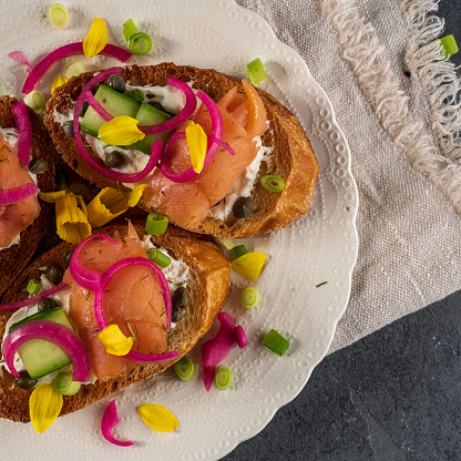 Crostini (toasted or grilled slices of French bread) with smoked salmon, cream cheese and cucumber. Garnished with pickled red onions, scallions, and daffodil petals.