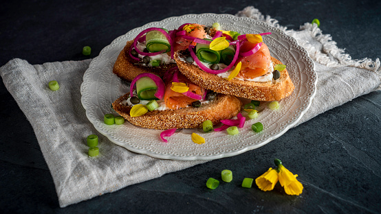 Crostini (toasted or grilled slices of French bread) with smoked salmon, cream cheese and cucumber. Garnished with pickled red onions, scallions, and daffodil petals.