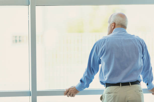 istock Mature man looks out of a large, bright, modern window 1488467507
