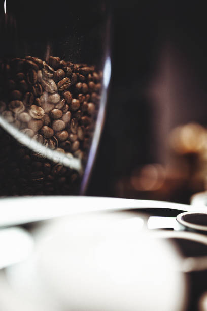 White cup filled with coffee beans and small red heart on wooden table with scattered beans and copy space on left. High quality photo