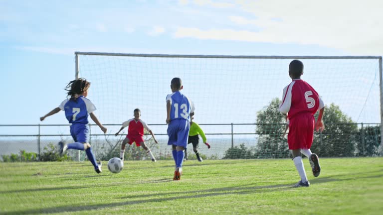 Football, sports and running with children playing on a field during a competitive team game in summer. Exercise, soccer and fitness with a group of kids outdoor together for a match on a grass pitch