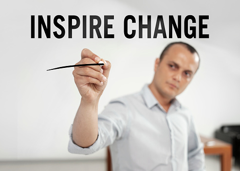 Businessman writing “Inspire change” text on a transparent wipe board in an office