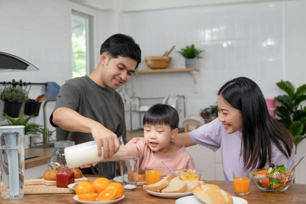 asian family breakfast at home. parents and children enjoy eating together, talking with laughter and good atmosphere. father plays with son playfully at kitchen table. - domestic life young family family child imagens e fotografias de stock