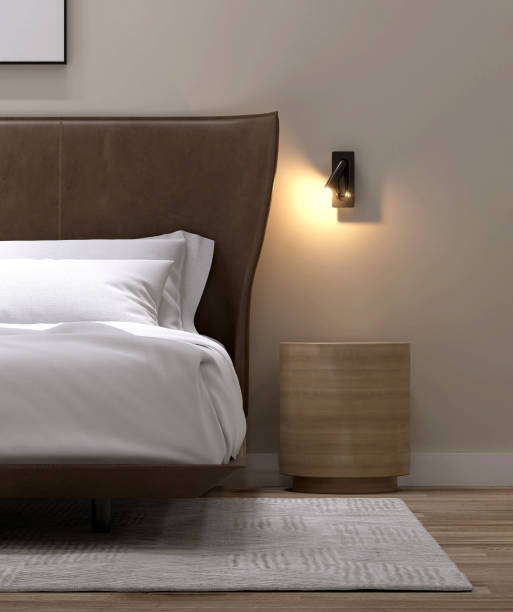istock Luxury, minimal round wooden bedside table, black spotlight, brown leather headboard bed, with white blanket, pillow, in elegant beige wall bedroom on parquet floor 1488490899
