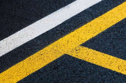 Road marking on brand new asphalt surface of a parking lot, yellow and white lines as abstract background in perspective