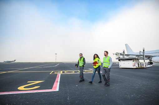 Diverse airport operatives in reflective vests standing at the airport runway looking at camera.